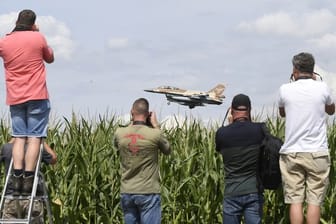 Ein israelischer F-16 Bomber landet auf dem Fliegerhorst Nörvenich im Kreis Düren, beobachtet von mehreren Männern mit Kameras, die an einem Maisfeld stehen.