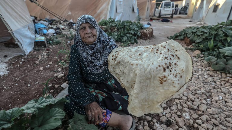 Ein Flüchtlingscamp in Syrien: Eine alte Frau blickt mit ihrem selbstgebackenen Brot in die Kamera.