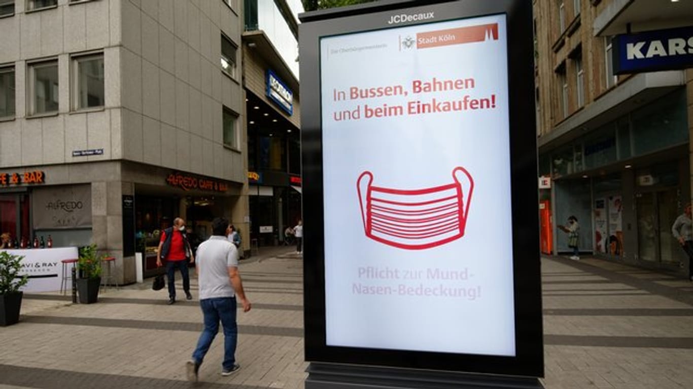 Ein Werbebildschirm weist in der Kölner Innenstadt auf die Maskenpflicht in Geschäften und im Nahverkehr hin.