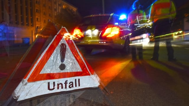 Ein Warndreieck mit dem Schriftzug "Unfall" steht vor einem Polizeifahrzeug.