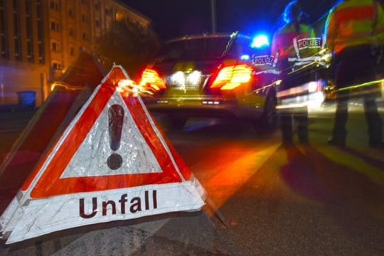 Ein Warndreieck mit dem Schriftzug "Unfall" steht vor einem Polizeifahrzeug.