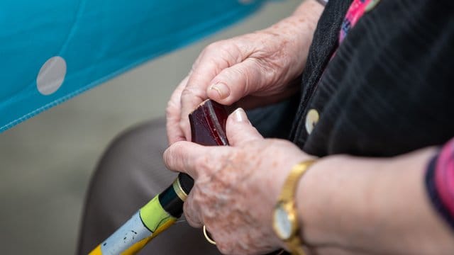 Eine Seniorin sitzt mit ihrem Gehstock im Garten eines Pflegeheims. Eine Seniorin sitzt mit ihrem Gehstock im Garten eines Pflegeheims.