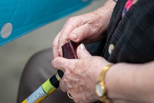Eine Seniorin sitzt mit ihrem Gehstock im Garten eines Pflegeheims.