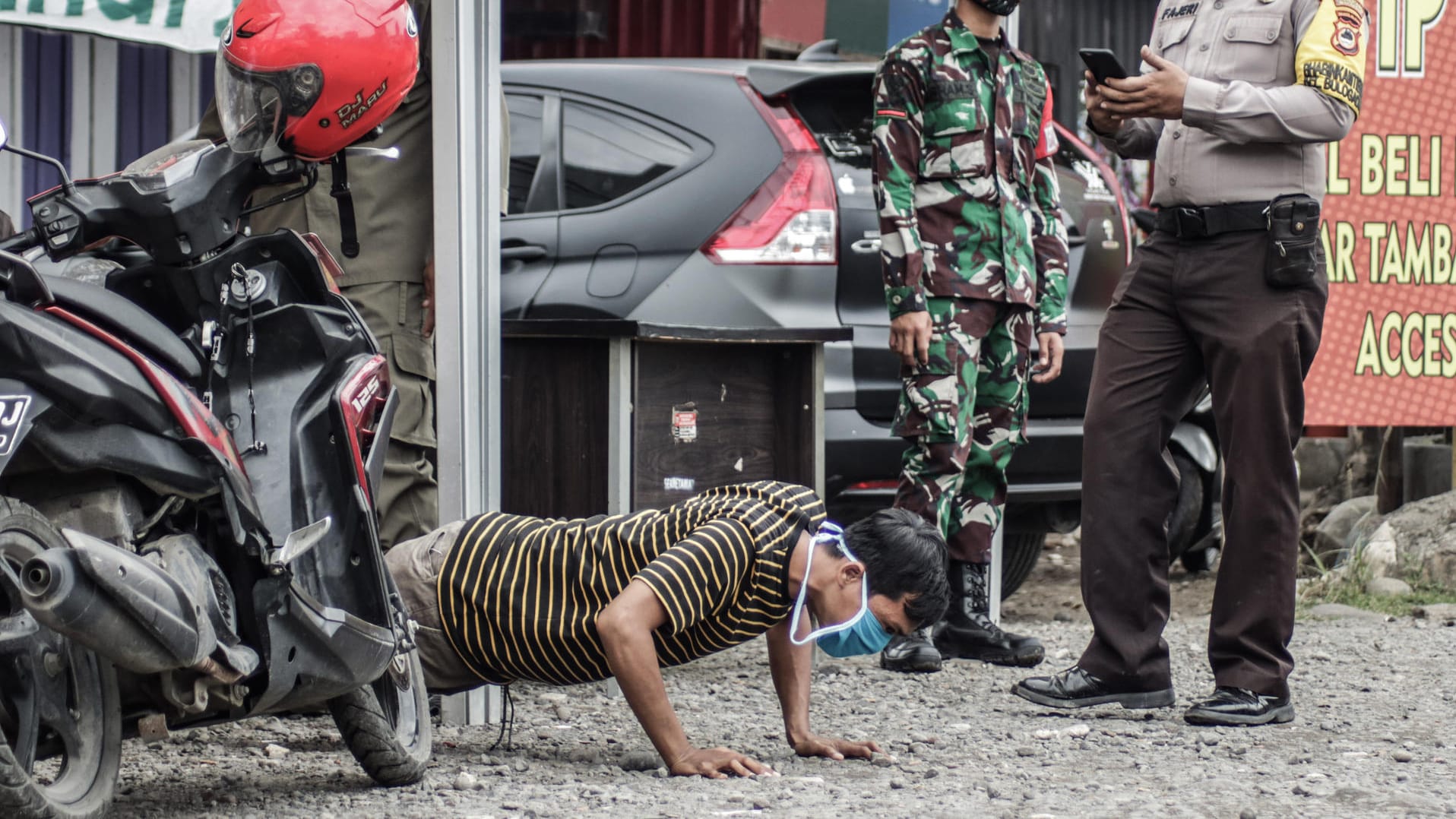 Indonesien, Makassar: Ein Motorradfahrer wird infolge der Missachtung von Corona-Schutzmaßnahmen von Polizeibeamten mit dem Durchführen von Push-Ups bestraft.