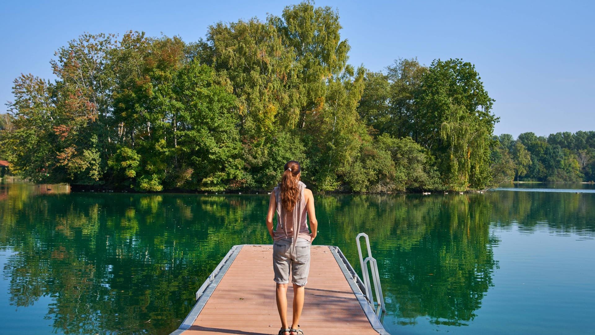 Junge Frau mit psychischer Krise steht auf einem Steg am See: Ängste kann man gut mit Atemübungen bekämpfen.