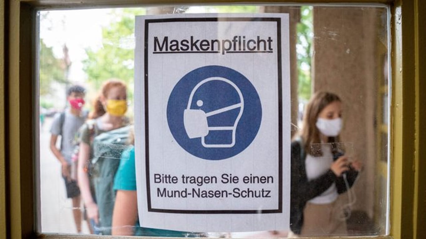 Schüler betreten hinter einem Plakat mit der Aufschrift "Maskenpflicht" am ersten Tag nach den Sommerferien den Eingang zum Rheingau Gymnasium in Berlin.
