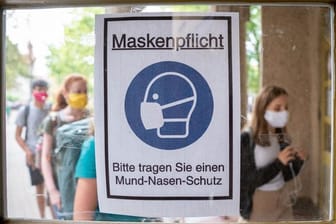 Schüler betreten hinter einem Plakat mit der Aufschrift "Maskenpflicht" am ersten Tag nach den Sommerferien den Eingang zum Rheingau Gymnasium in Berlin.