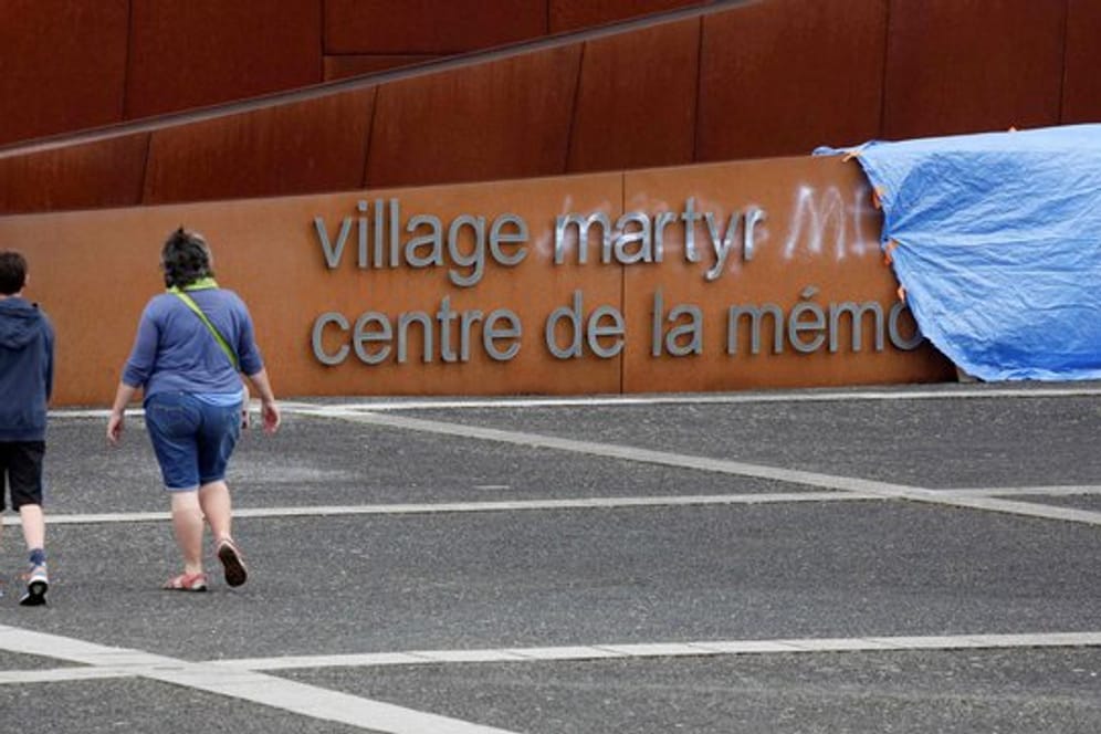 Besucher gehen an einem abgedeckten Graffiti auf dem Schriftzug am Eingang der Gedenkstätte in Oradour-sur-Glane vorbei.