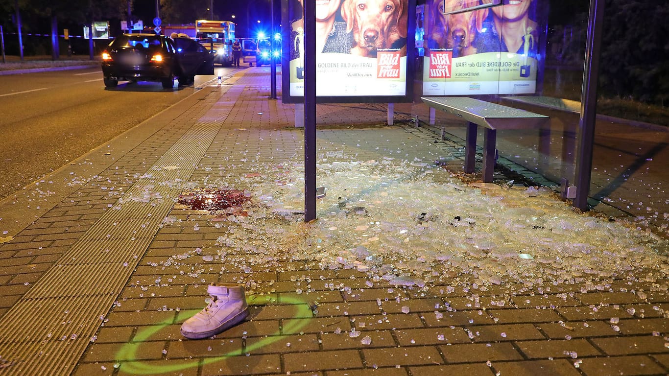 Sachsen, Dresden: Ein einzelner Sportschuh liegt nach einem Verkehrsunfall an einer Bushaltestelle zwischen Glasscherben in einem Farbkreis der Spurensicherung der Polizei.