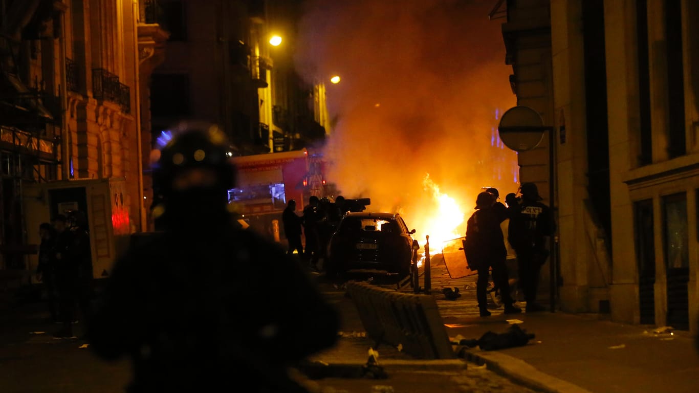 Polizisten beobachten ein brennendes Auto in der Nähe der Champs-Elysee-Allee: Nach dem 1:0-Sieg des FC Bayern gegen Paris Saint-Germain ist es in der französischen Hauptstadt zu Ausschreitungen gekommen.