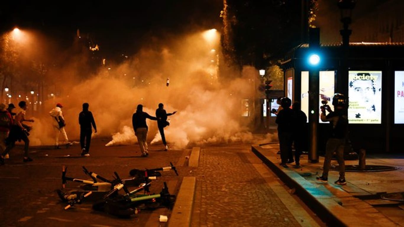 Fans von Paris Saint-Germain treten auf der Champs-Elysées gegen Tränengaskanister.