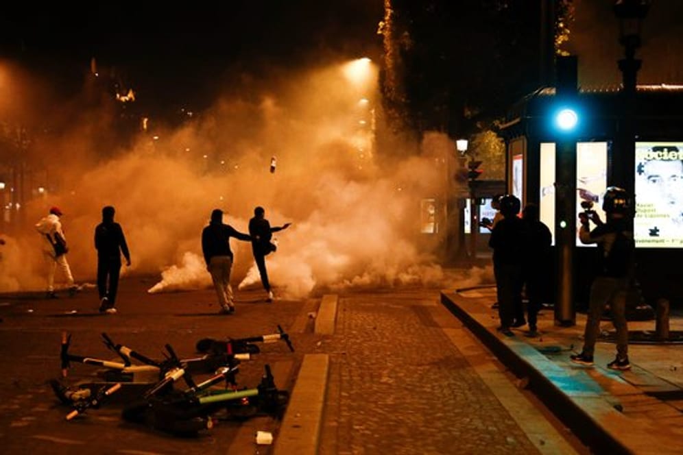 Fans von Paris Saint-Germain treten auf der Champs-Elysées gegen Tränengaskanister.