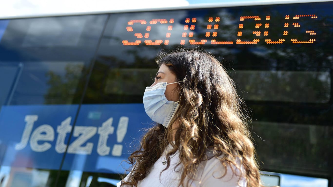 Eine Schülerin wartet mit Maske vor einem Schulbus (Symbolbild): In Bielefeld waren einige Busse zeitweise zu voll, das soll nun geändert werden.