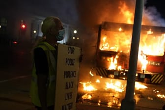 Ein Demonstrant steht mit einem Transparentvor einem brennenden Müllwagen.