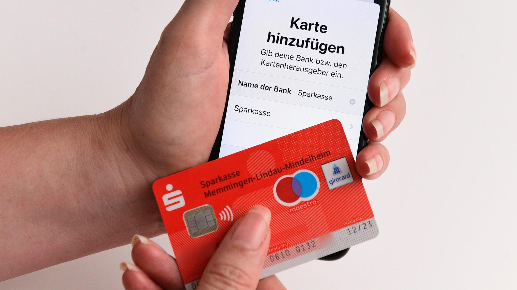 Eine Girocard der Sparkasse vor einem iPhone: Apple Pay ist jetzt auch für Girocards der Sparkasse verfügbar.