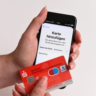 Eine Girocard der Sparkasse vor einem iPhone: Apple Pay ist jetzt auch für Girocards der Sparkasse verfügbar.