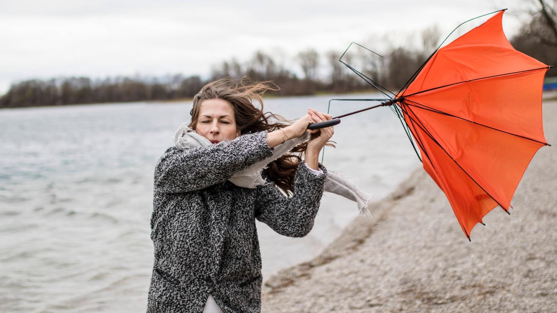 Eine Frau hält einen Regenschirm, der im Sturm umgestülpt wurde (Symbolbild): Wegen der Sturms "Kirsten" sind in Erfurt unter anderem die Friedhöfe geschlossen worden.