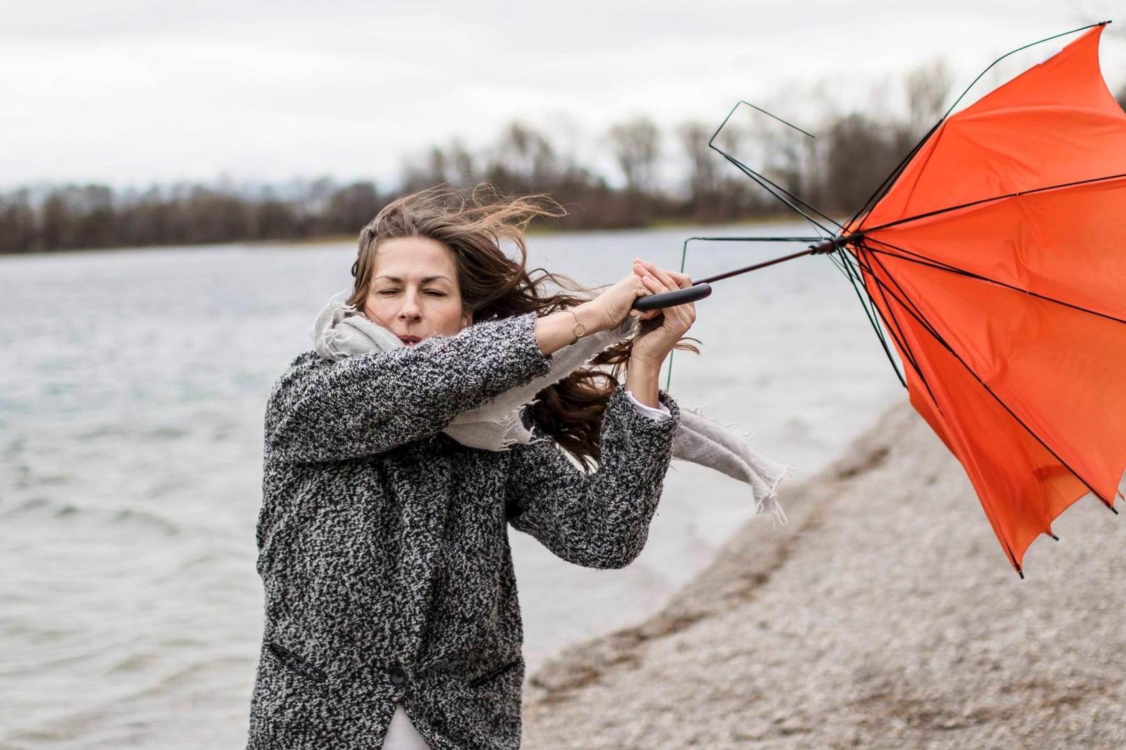 Eine Frau hält einen Regenschirm, der im Sturm umgestülpt wurde (Symbolbild): Wegen der Sturms "Kirsten" sind in Erfurt unter anderem die Friedhöfe geschlossen worden.