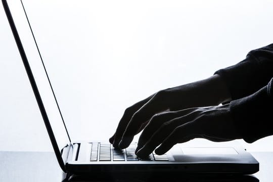 Ein Mann tippt auf einer Tastatur eines Laptops.