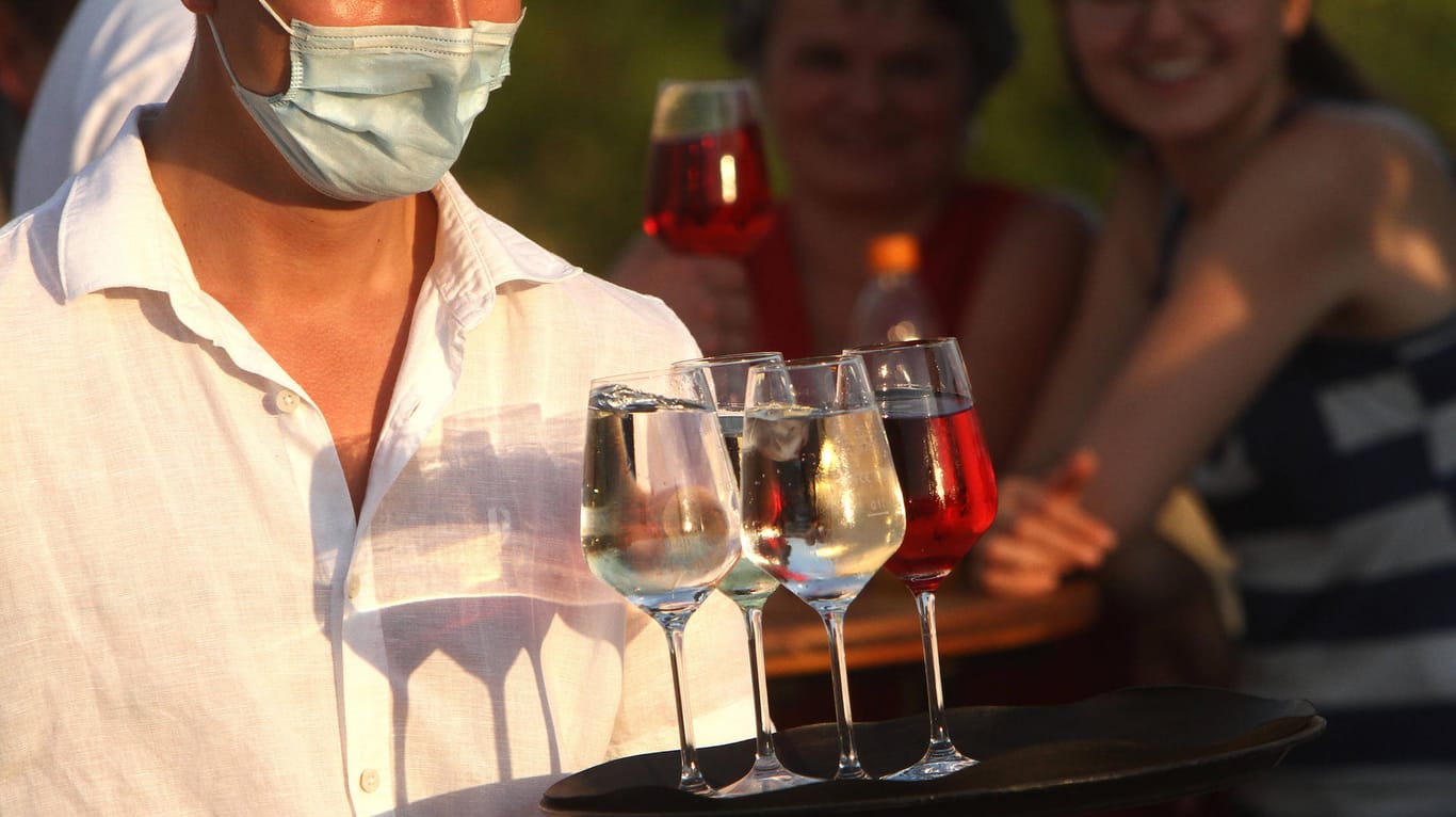 Ein Kellner mit Maske trägt Wein auf einem Tablett: In Wuppertal kommt es in der Gastronomie offenbar regelmäßig zu Corona-Verstößen.