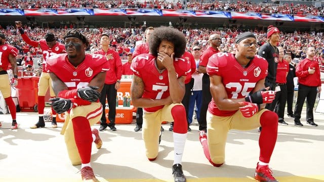 Colin Kaepernick (M), Eli Harold (l) und Eric Reid von den San Francisco 49ers knien 2016 beim Abspielen der US-Nationalhymne.