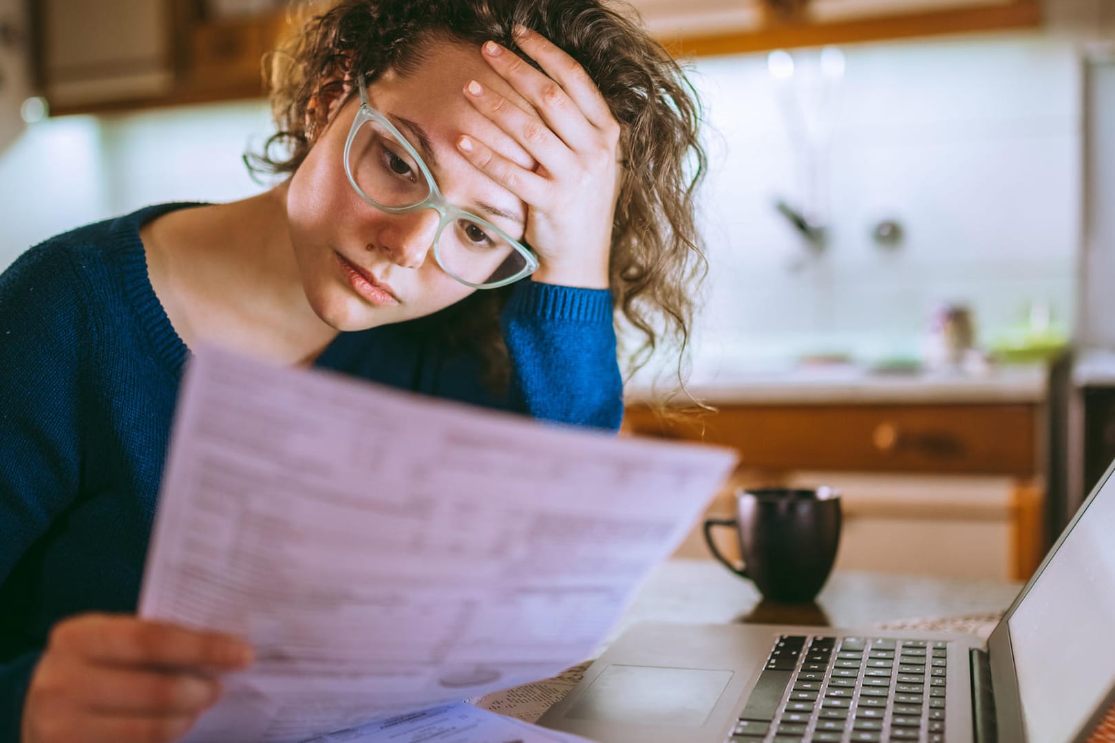 Eine junge Frau blickt gestresst auf eine Rechnung (Symbolbild): Immer mehr Banken verlangen einen Negativzins.