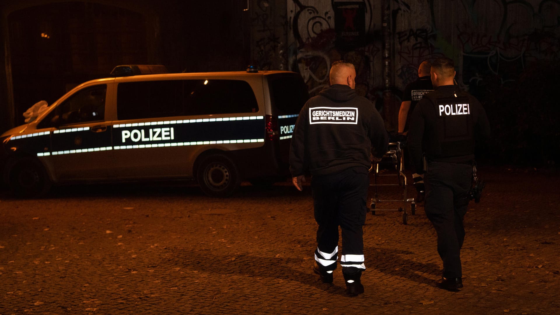 Ein Polizist und ein Gerichtsmediziner gehen zu einem Einsatzfahrzeug der Polizei im Monbijoupark in Berlin-Mitte (Archivbild): Ein Begleiter des Jugendlichen wurde erheblich verletzt.