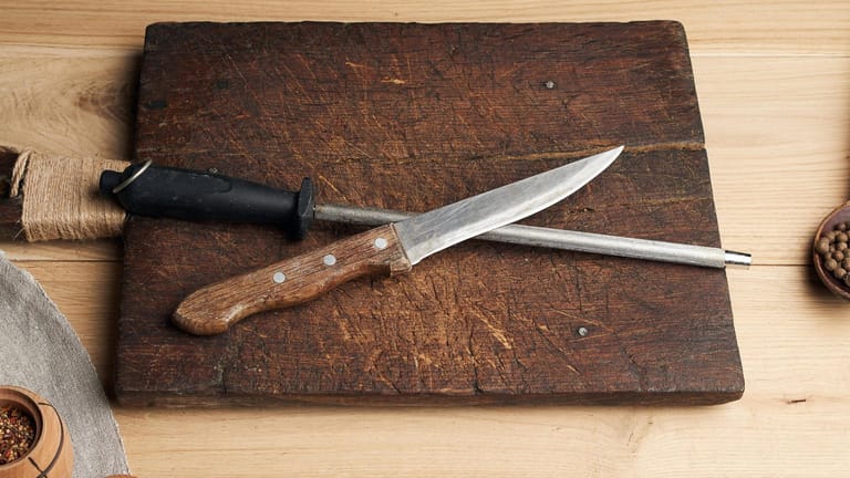 Ein Wetzstab und Messer liegen auf einem Schneidebrett aus Holz.
