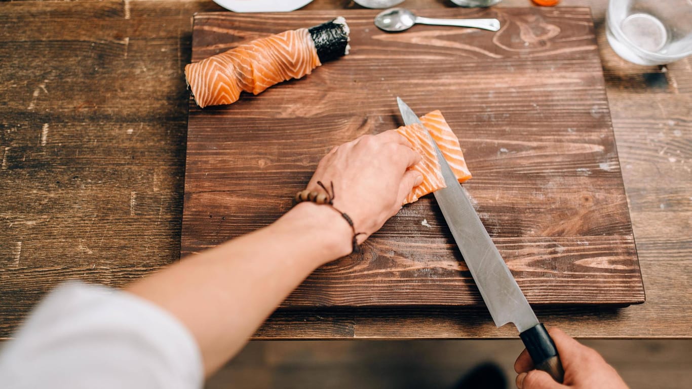 Ein Mann bereitet Sushi zu und schneidet mit dem Messer in ein Lachsfilet.