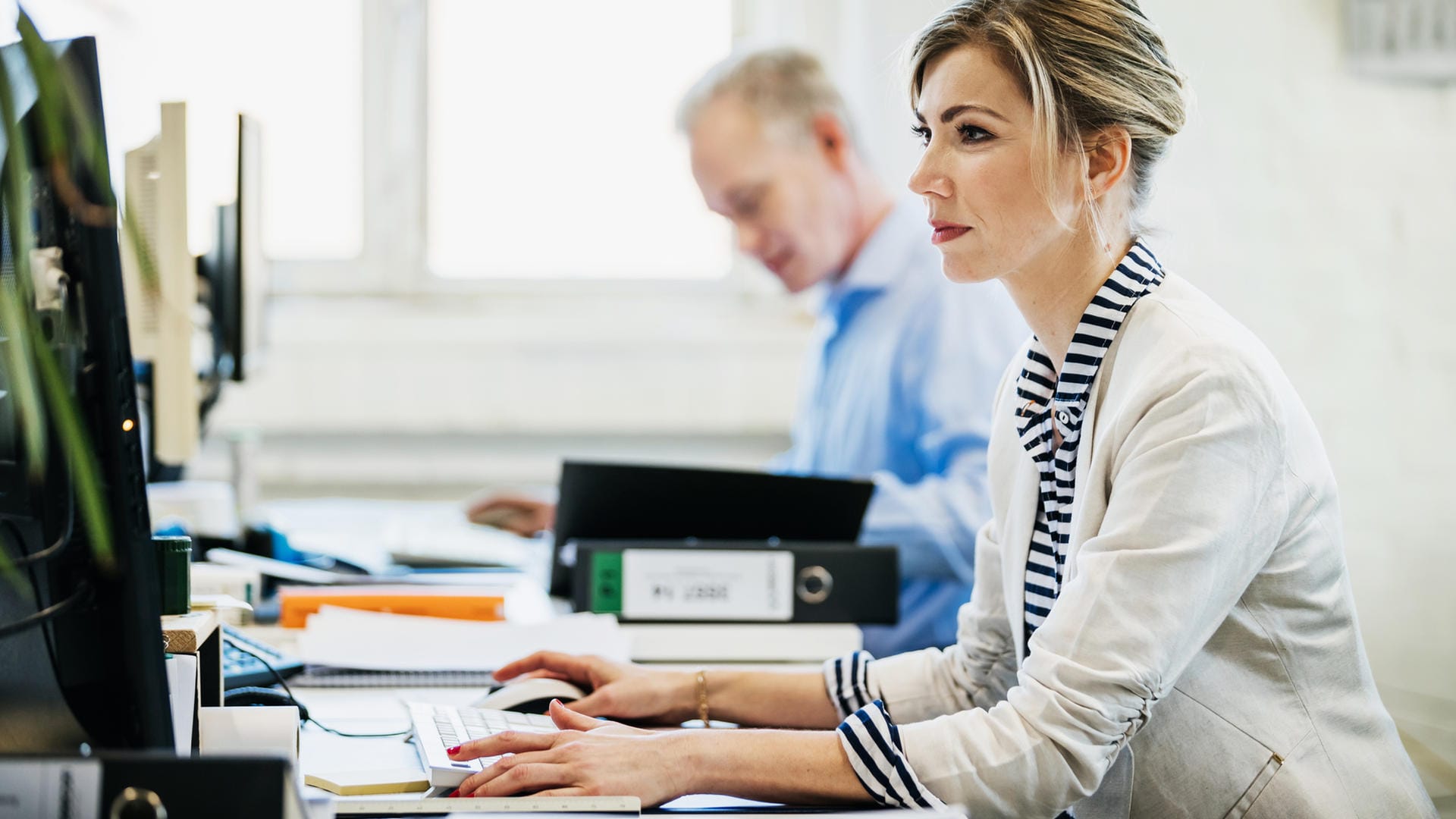 Arbeitskollegen sitzen am Schreibtisch (Symbolbild): Trotz Entgeltgleichheitsgebot verdienen Frauen im gleichen Job weniger Geld.