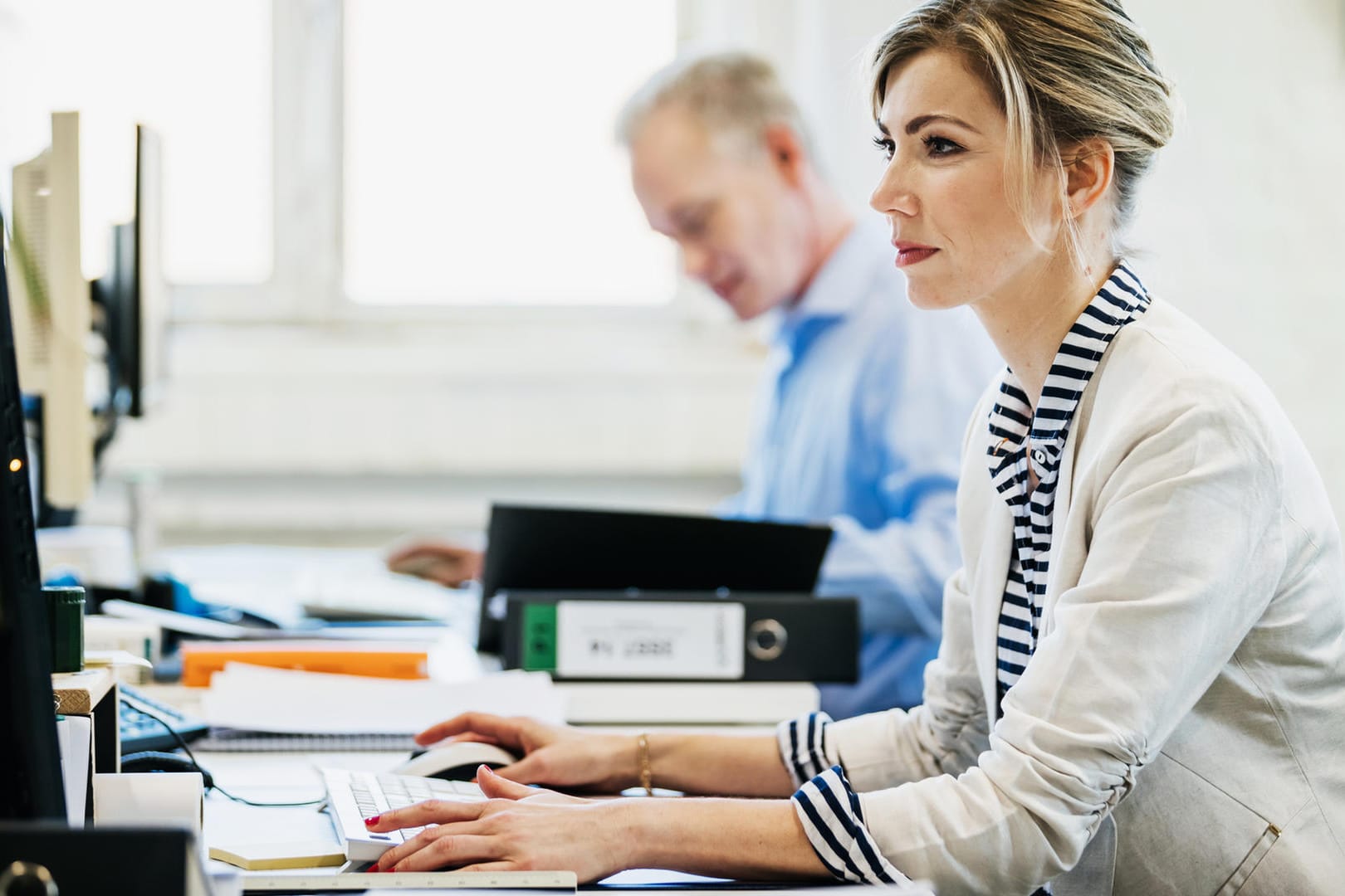 Arbeitskollegen sitzen am Schreibtisch (Symbolbild): Trotz Entgeltgleichheitsgebot verdienen Frauen im gleichen Job weniger Geld.