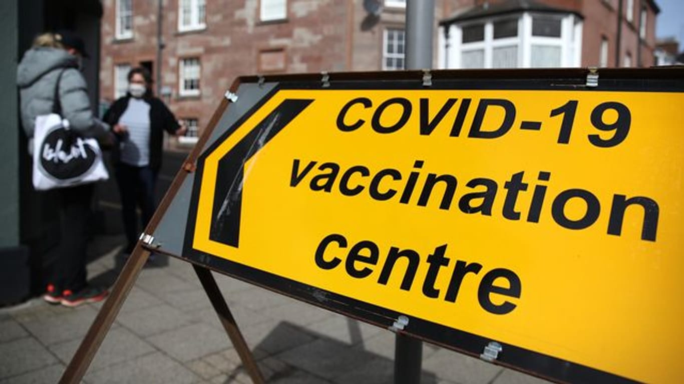 Hinter einem Schild eines Corona-Impfzentrums in Blairgowrie stehen zwei Menschen mit Mund-Nasen-Schutz.