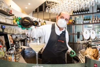 Ein Barmann mit Atemschutzmaske schenkt in Bozen ein Glas Wein ein.