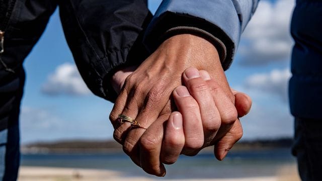 Eine Frau und ein Mann halten sich bei einem Strandspaziergang an den Händen.