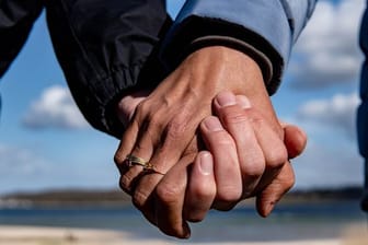 Eine Frau und ein Mann halten sich bei einem Strandspaziergang an den Händen.