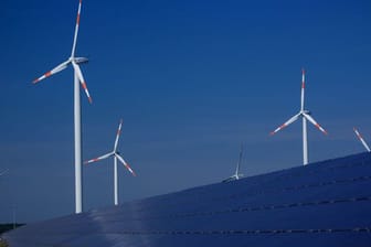 Windräder zur Stromerzeugung drehen sich in Mecklenburg-Vorpommern hinter einem Solarpark.
