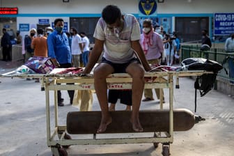 Ein Mann wartet auf einer Liege vor einem Krankenhaus: Die meisten Betten sind belegt.