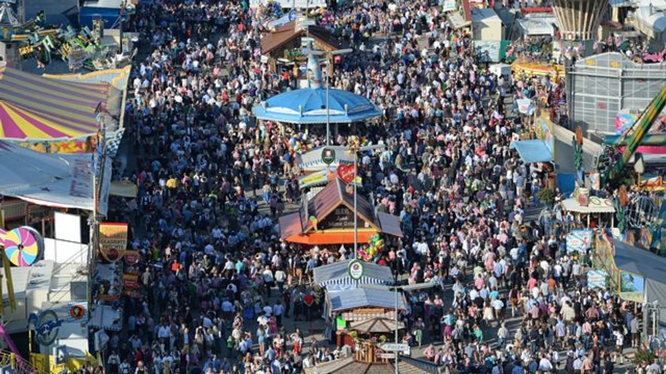 Zahlreiche Menschen gehen bei Sonnenschein über das Oktoberfest-Gelände in München.