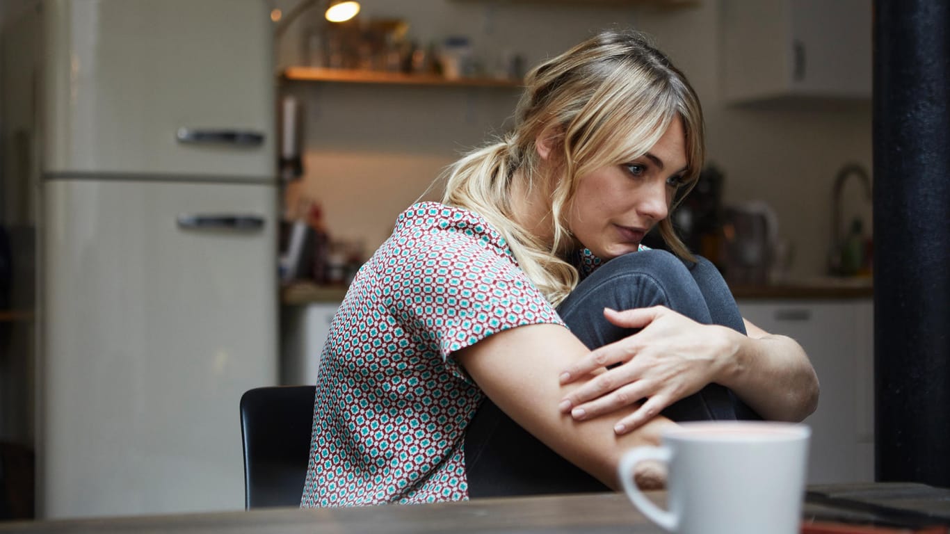 Eine Frau sitzt nachdenklich am Küchentisch: Häufige Stimmungswechsel können körperliche und psychische Ursachen haben.
