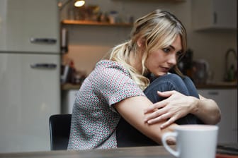 Eine Frau sitzt nachdenklich am Küchentisch: Häufige Stimmungswechsel können körperliche und psychische Ursachen haben.