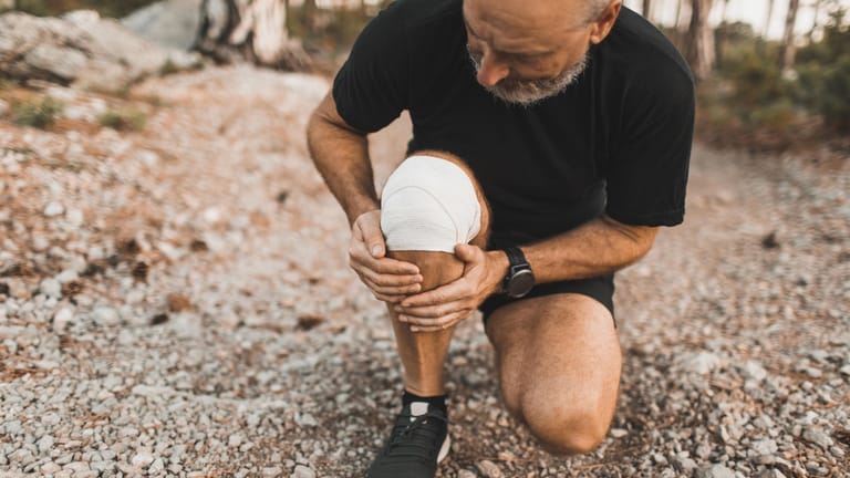Ein Mann mit Kniebandage greift sich an die Wade. Sportliche Aktivitäten sind wichtig, um im alter fit zu bleiben. Überlastungen sollte man jedoch vermeiden.