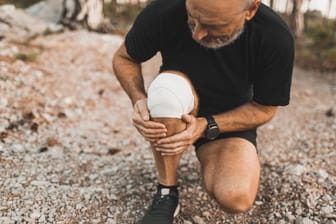 Ein Mann mit Kniebandage greift sich an die Wade. Sportliche Aktivitäten sind wichtig, um im alter fit zu bleiben. Überlastungen sollte man jedoch vermeiden.
