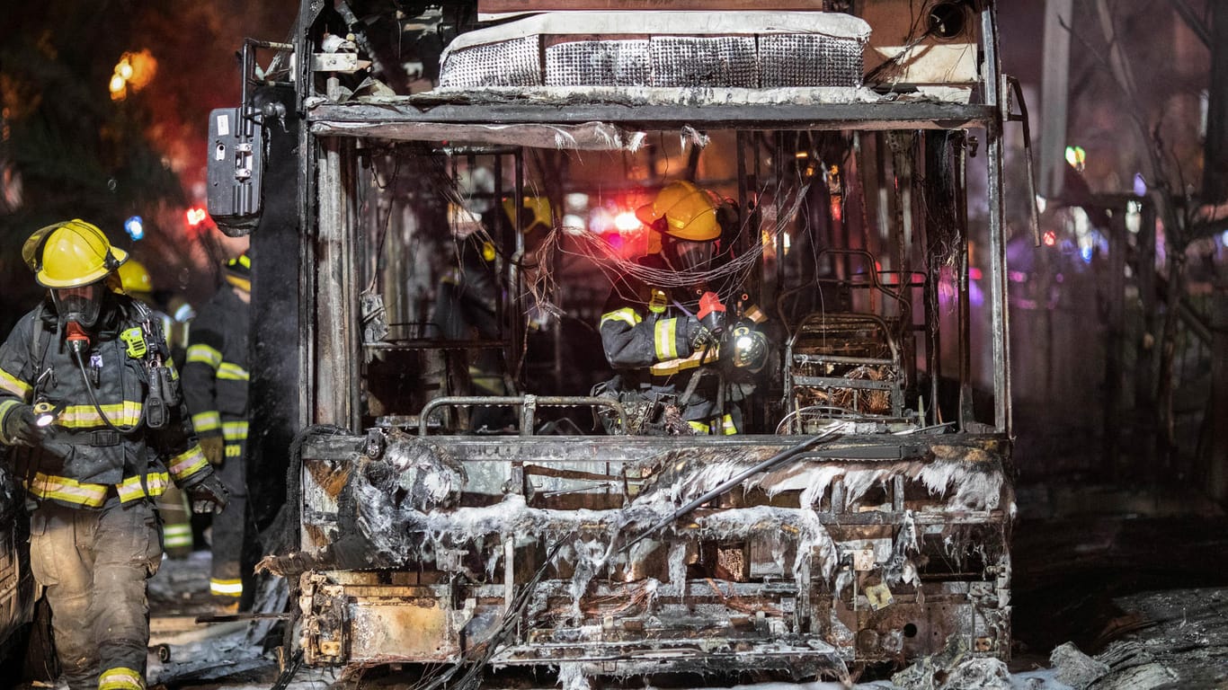 Israel, Holon: Israelische Feuerwehrleute inspizieren einen verbrannten Bus, nachdem dieser von einer Rakete aus dem Gazastreifen getroffen wurde.