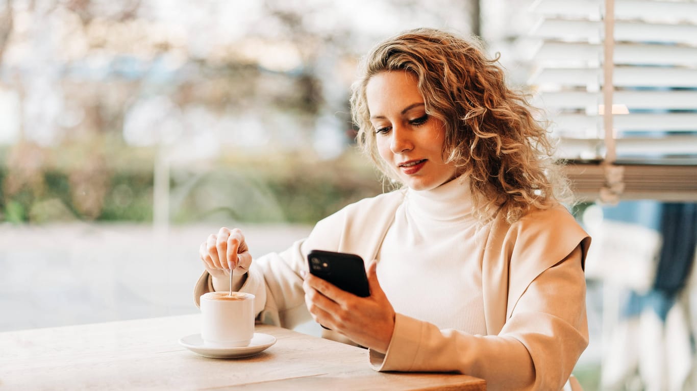 Eine Frau sitzt mit ihrem Smartphone in einem Café (Symbolbild): Die Kölner App "MeineCheckins" soll die Kontaktverfolgung erleichtern.