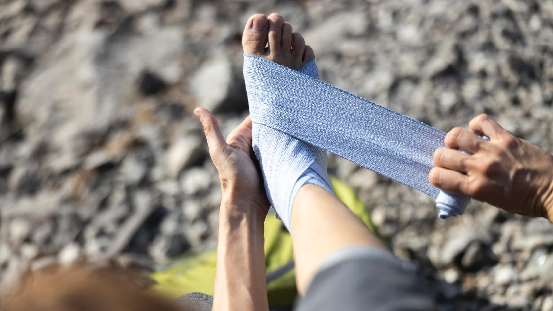 Eine Frau bindet sich eine Bandage um den Fuß: Auf längeren Wandertouren empfiehlt es sich, eine Erste-Hilfe-Grundausstattung mitzunehmen.