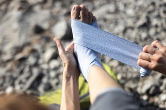 Eine Frau bindet sich eine Bandage um den Fuß: Auf längeren Wandertouren empfiehlt es sich, eine Erste-Hilfe-Grundausstattung mitzunehmen.