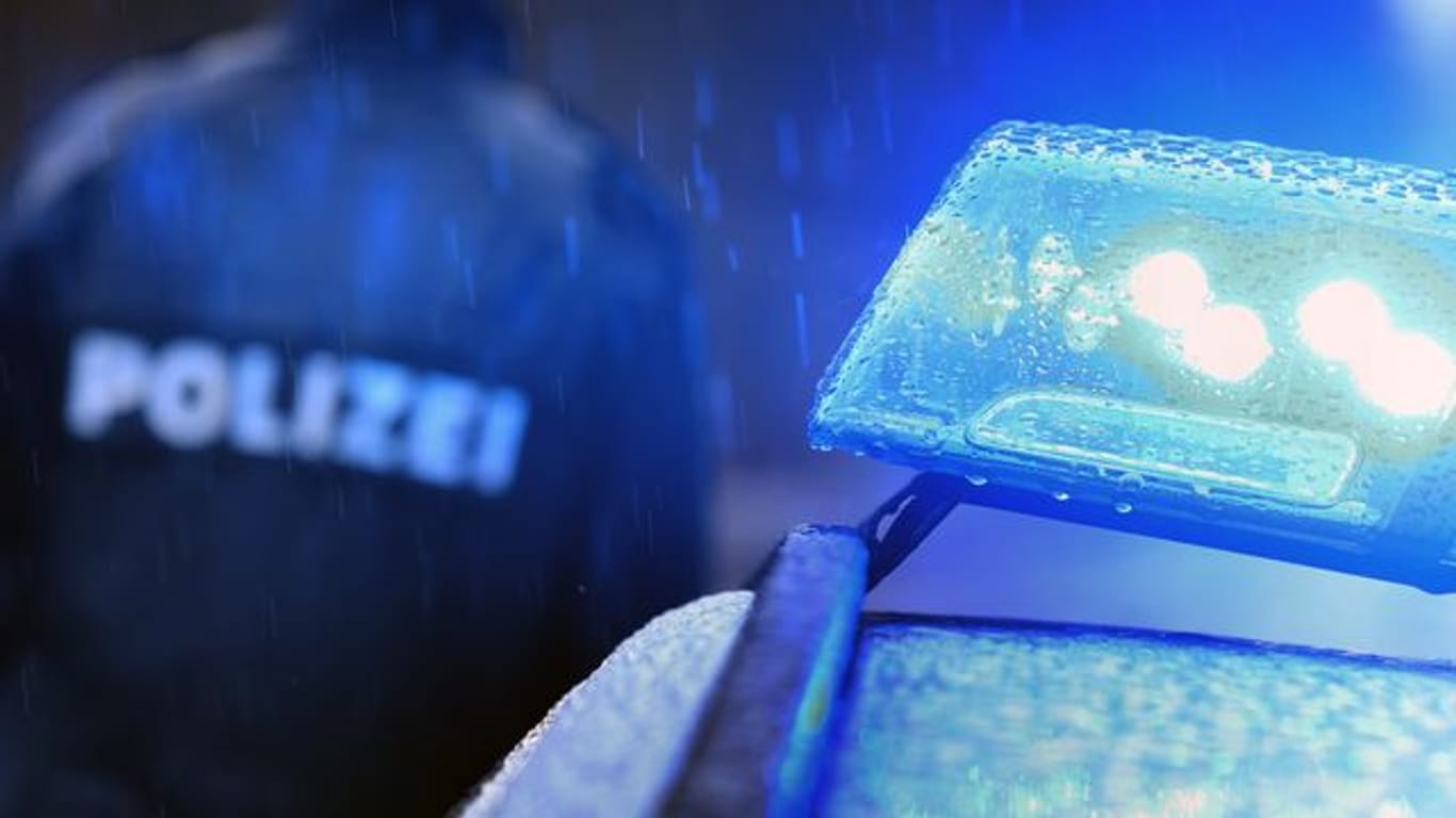 Ein Polizist steht vor einem Streifenwagen mit Blaulicht (Symbolbild): In Frankfurt ist ein Passant ausgeraubt worden. Die Täter gingen dabei brutal vor.