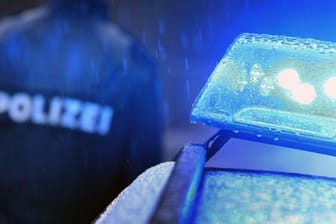 Ein Polizist steht vor einem Streifenwagen mit Blaulicht (Symbolbild): In Frankfurt ist ein Passant ausgeraubt worden. Die Täter gingen dabei brutal vor.