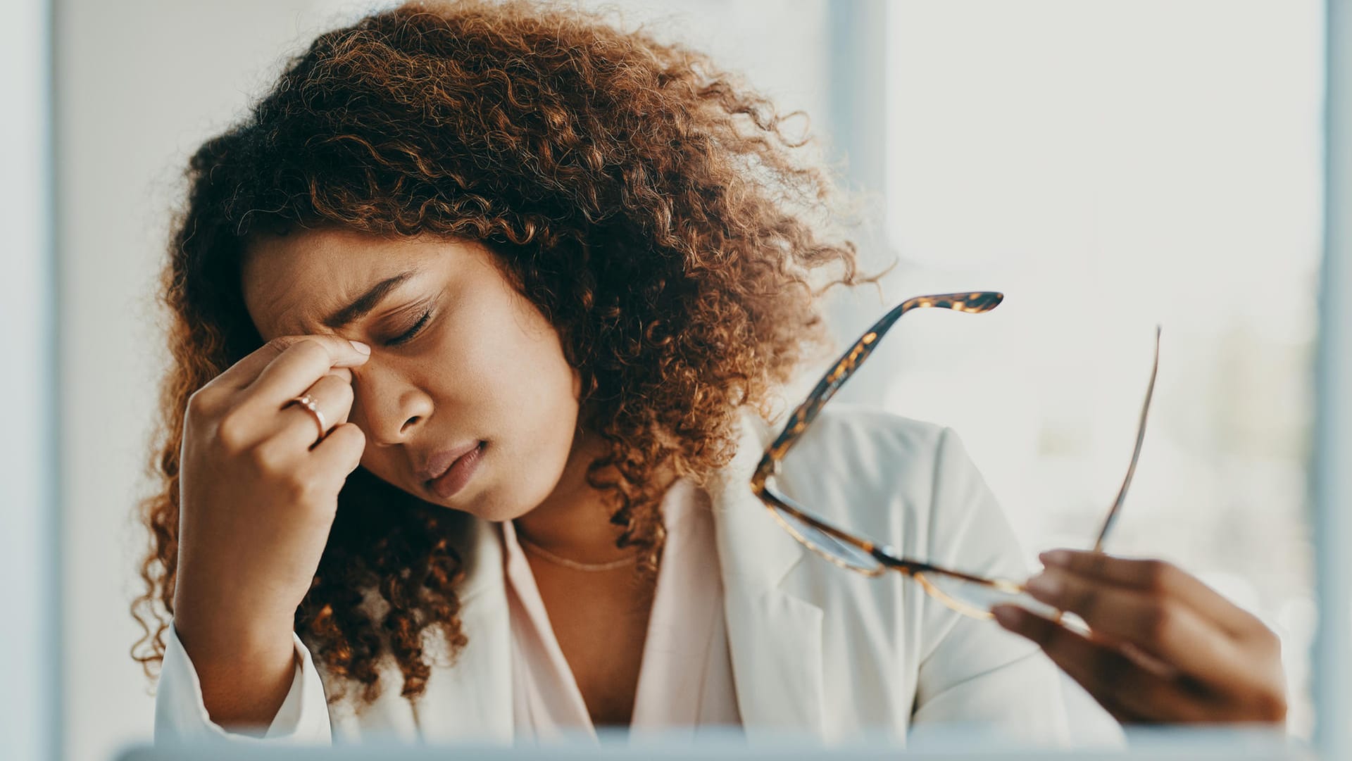 Erschöpfte Frau vor einem Computer-Display. Müde, brennende Augen sind ein Warnzeichen, dass die Augen zu trocken sind und eine Pause brauchen.