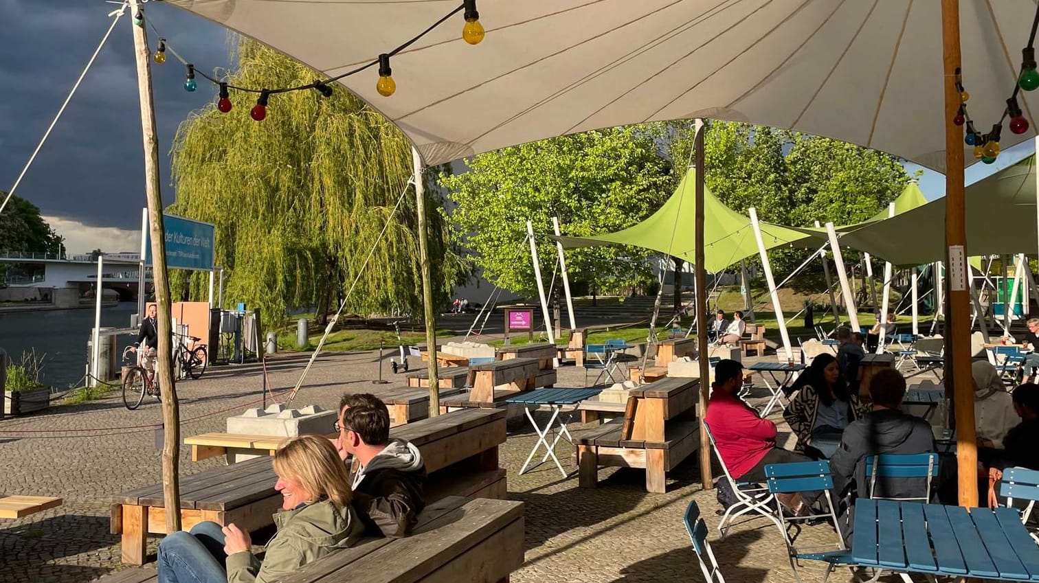 Menschen sitzen am Haus der Kulturen der Welt an Tischen: Am Abend hatte es vereinzelte Schauer gegeben, zudem war es recht stürmisch.